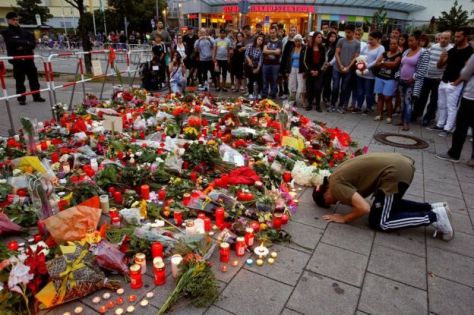 A man prays beside flowers laid in front of the Olympia shopping mall in Munich, Germany, 23 July